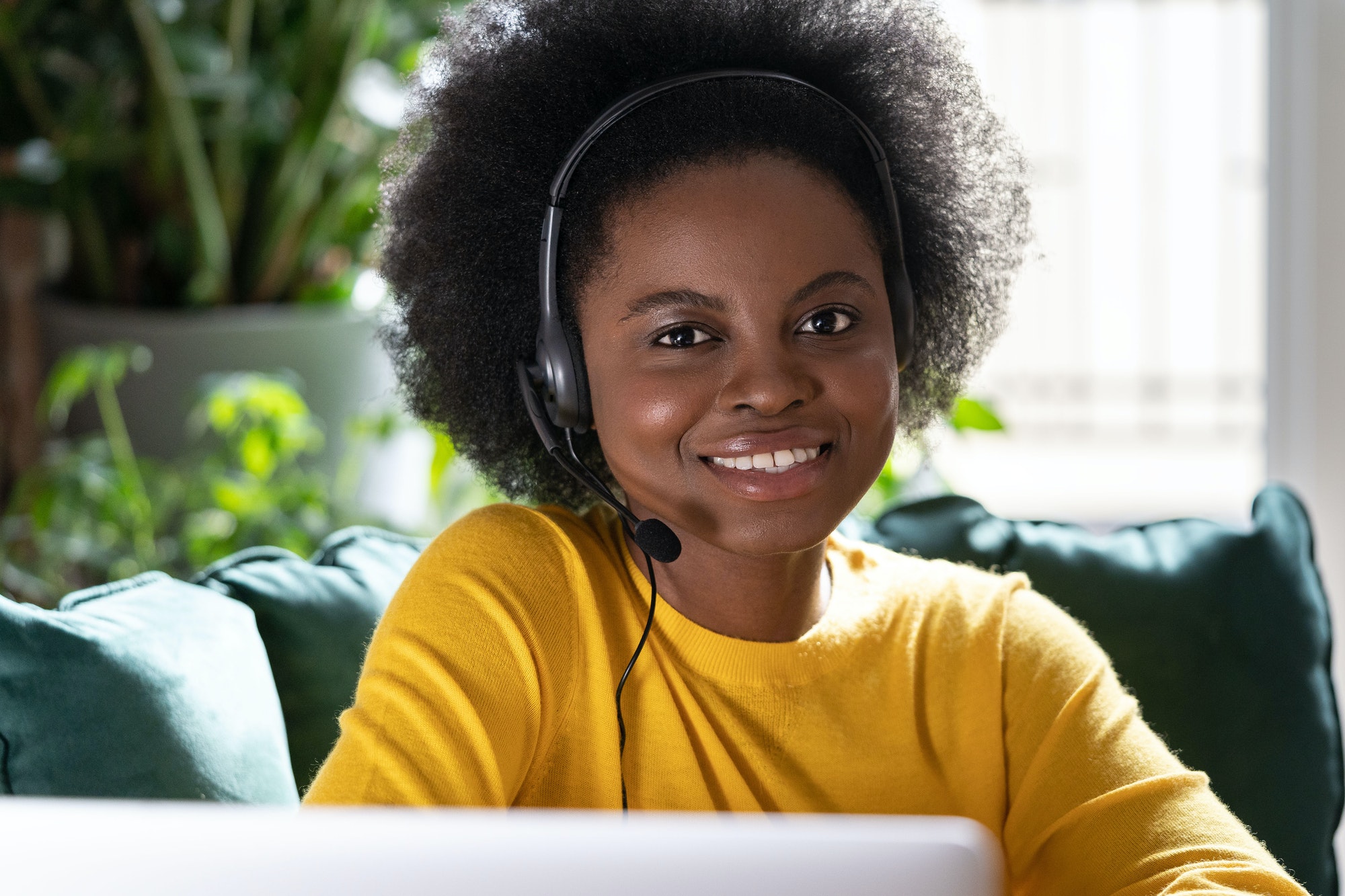 Smiling African consultant woman wear headphones looking at camera remote work on laptop. E-business